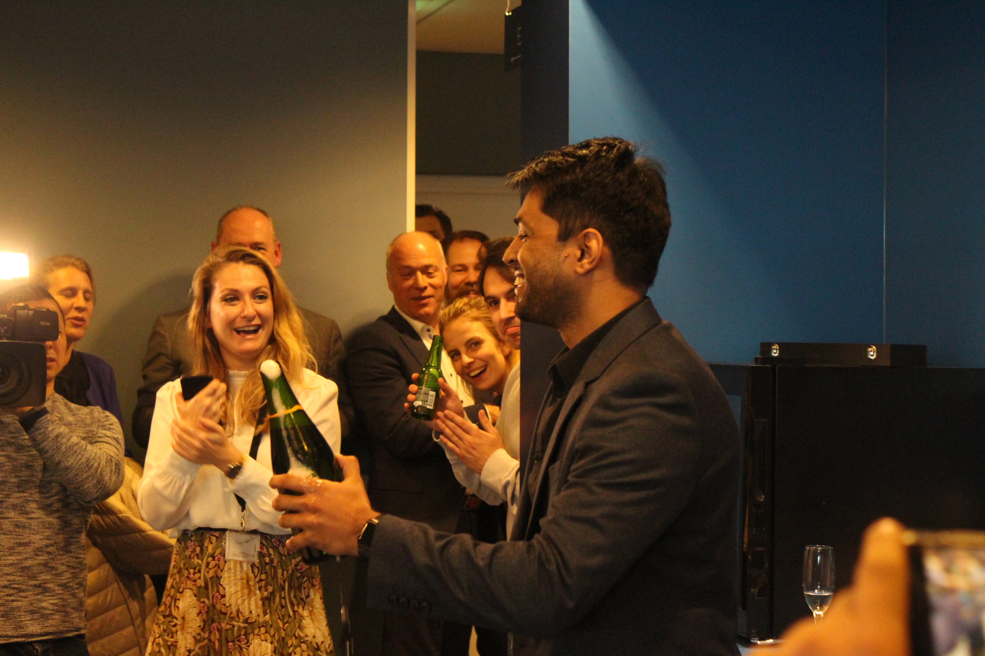 Co-founder Karthik Mahadevan holds the open champagne bottle and smiles. 