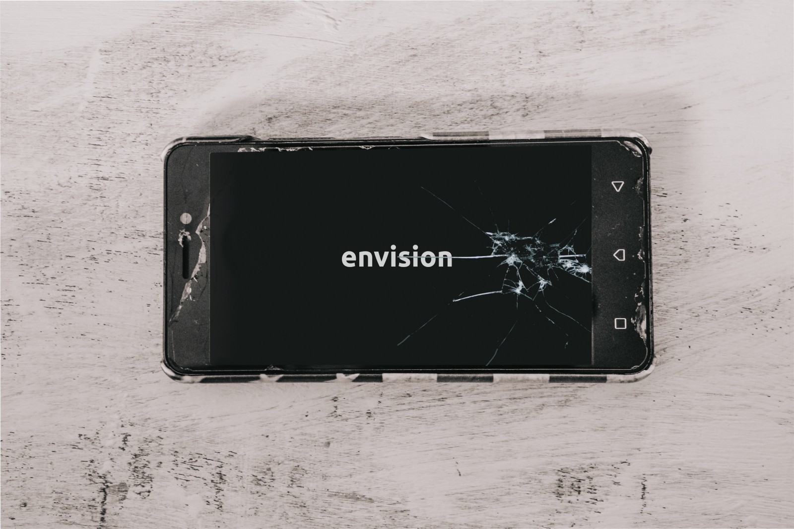 A picture of a smartphone on a table with multiple cracks on it with the text on screen reading “Envision”