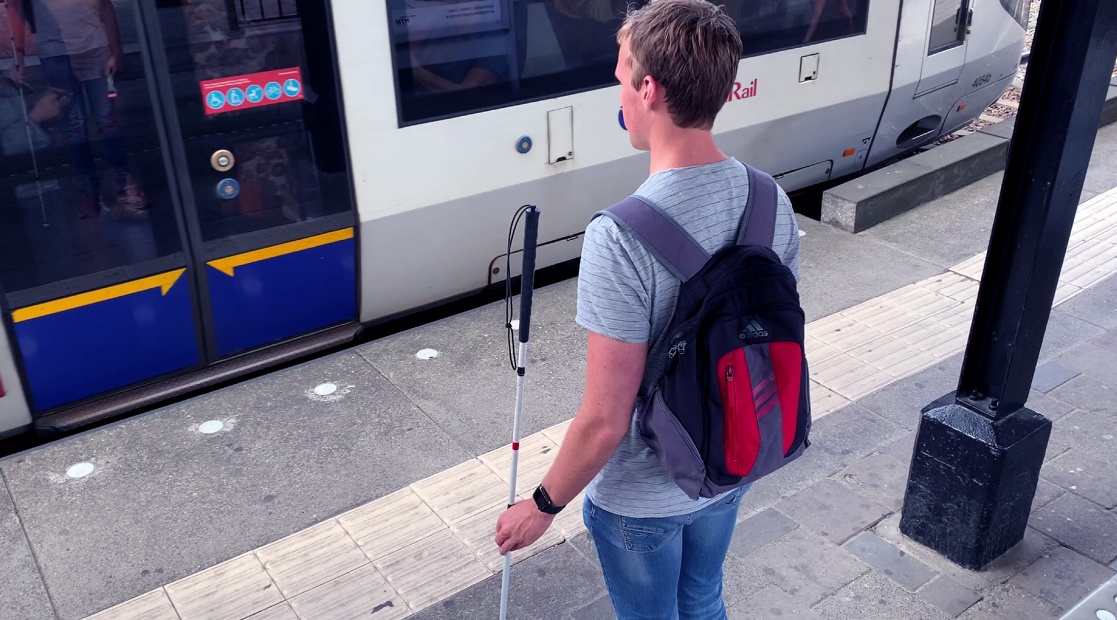 Jesse standing in front of a train at the station holding a cane.
