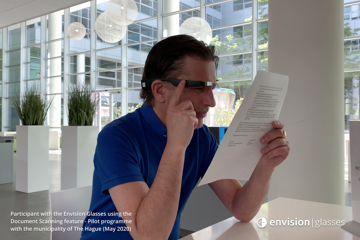 A participant of the pilot programme using the document scanning feature of the Envision Glasses while holding tapping with his right finger on the Envision Glasses and holding a document with his left hand.