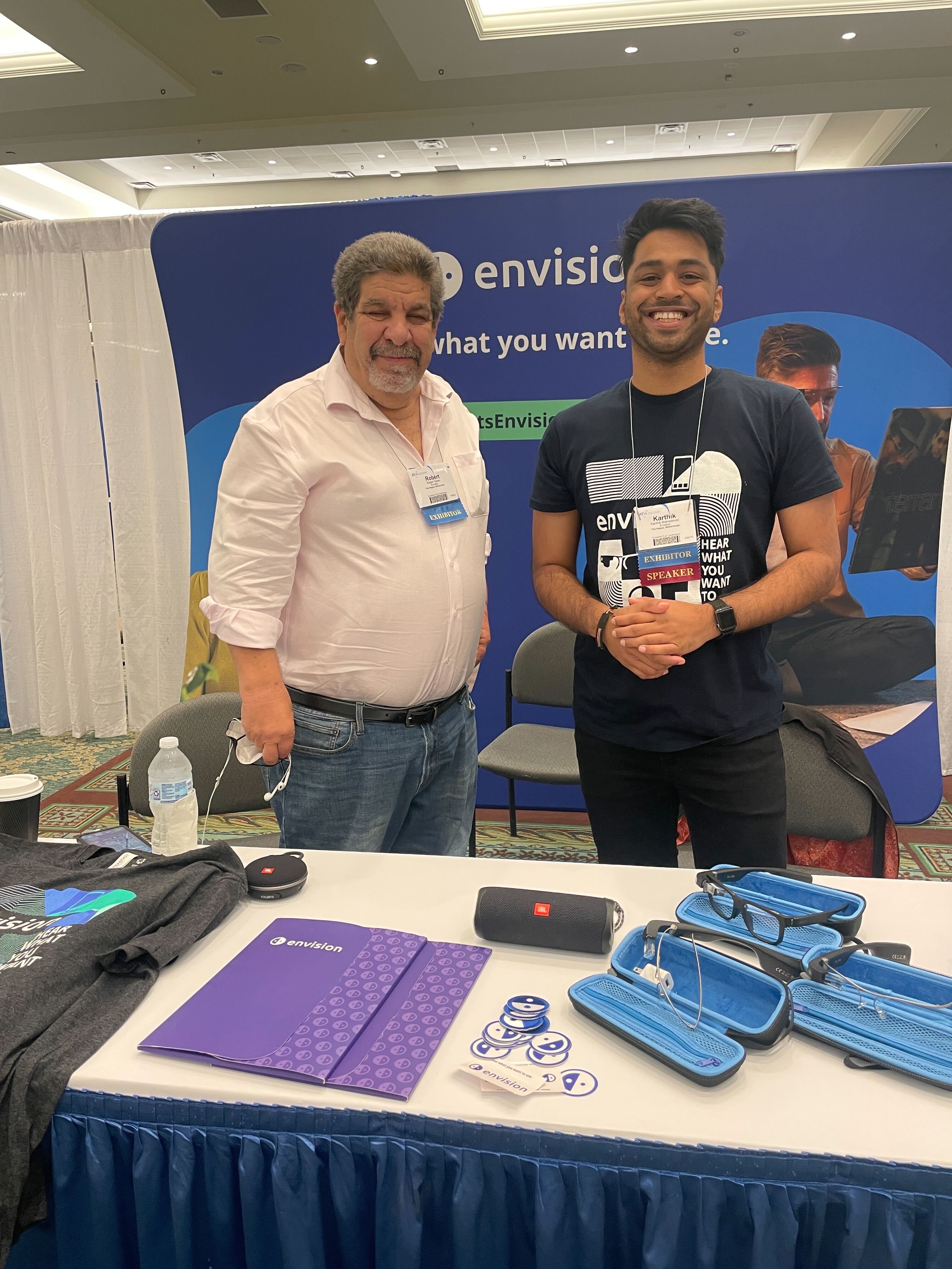 Robert and Karthik from Envision, standing in front of our booth and smiling for the camera.
