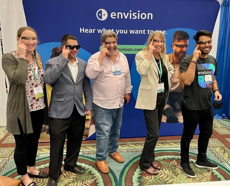 Annika (from Florida Vision Technology), Jose (from Florida Vision Technology), Robert (from Envision), Lesa (from Florida Vision Technology) and Karthik (from Envision) wearing the Envision Glasses and posing for a picture at our booth.