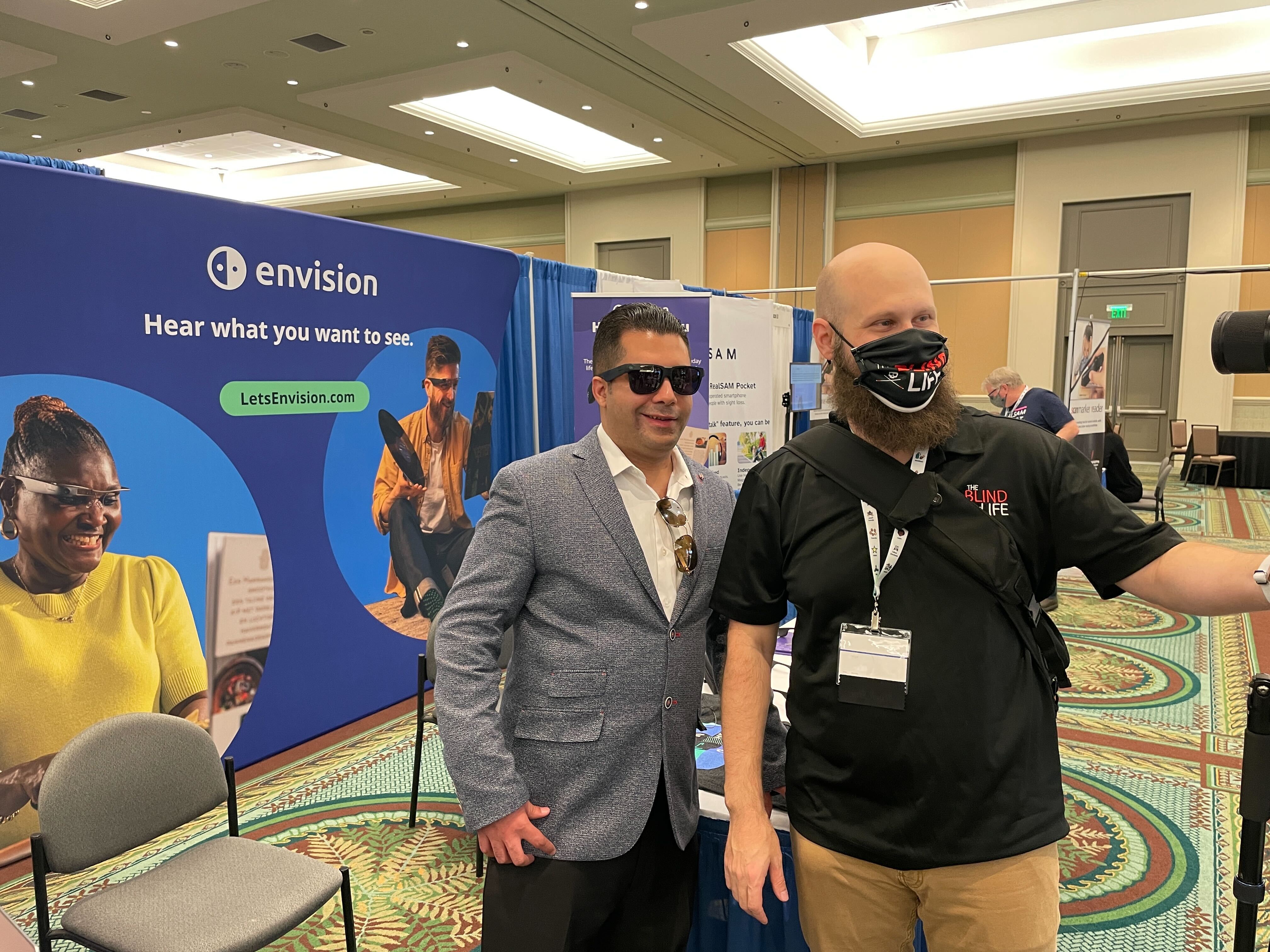 Sam from The Blind Life taking a selfie in front of the Envision booth with Jose.