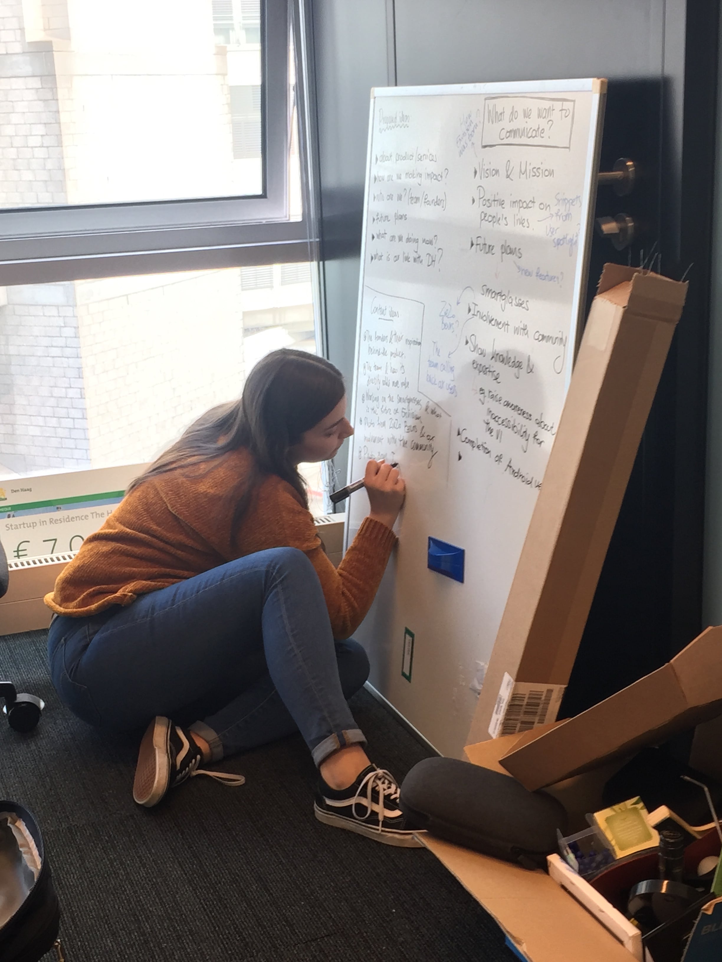 Dafni writing down her marketing ideas on a whiteboard while sitting on the floor