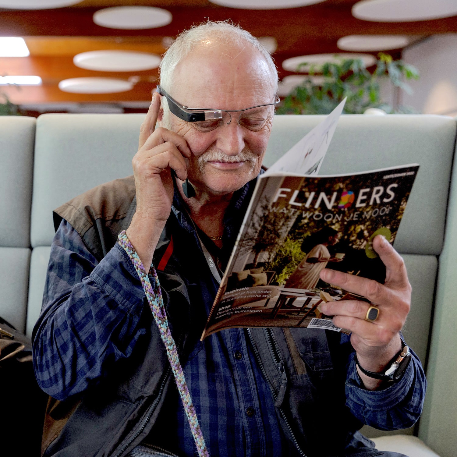 A man wearing Envision Glasses and holding a magazine
