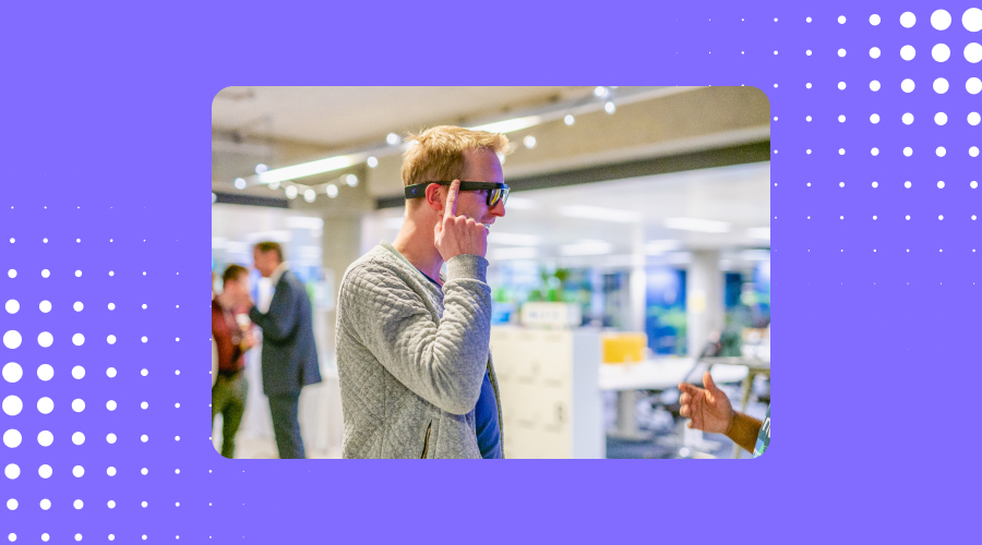 Photo of a person using the Envision Glasses, the photo is inside a blue frame with branded dots on the top-right and bottom-left corner.