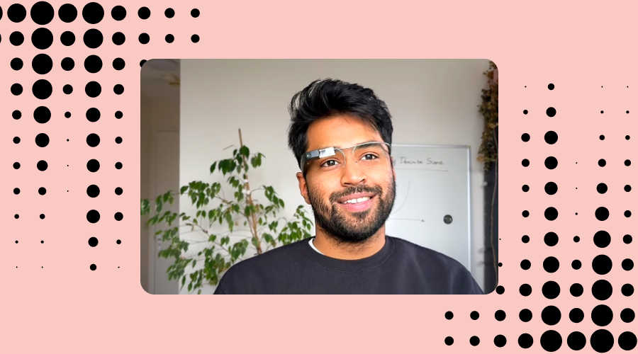A man with a cheerful smile, identified as Karthik Mahadevan, CEO and co-founder at Envision, is wearing Envision glasses. In the background, there is a 'Describe Scene Evolution' graph on a whiteboard. The image has a decorative border with a pattern of black dots on a pink background, indicative of Envision's branding.