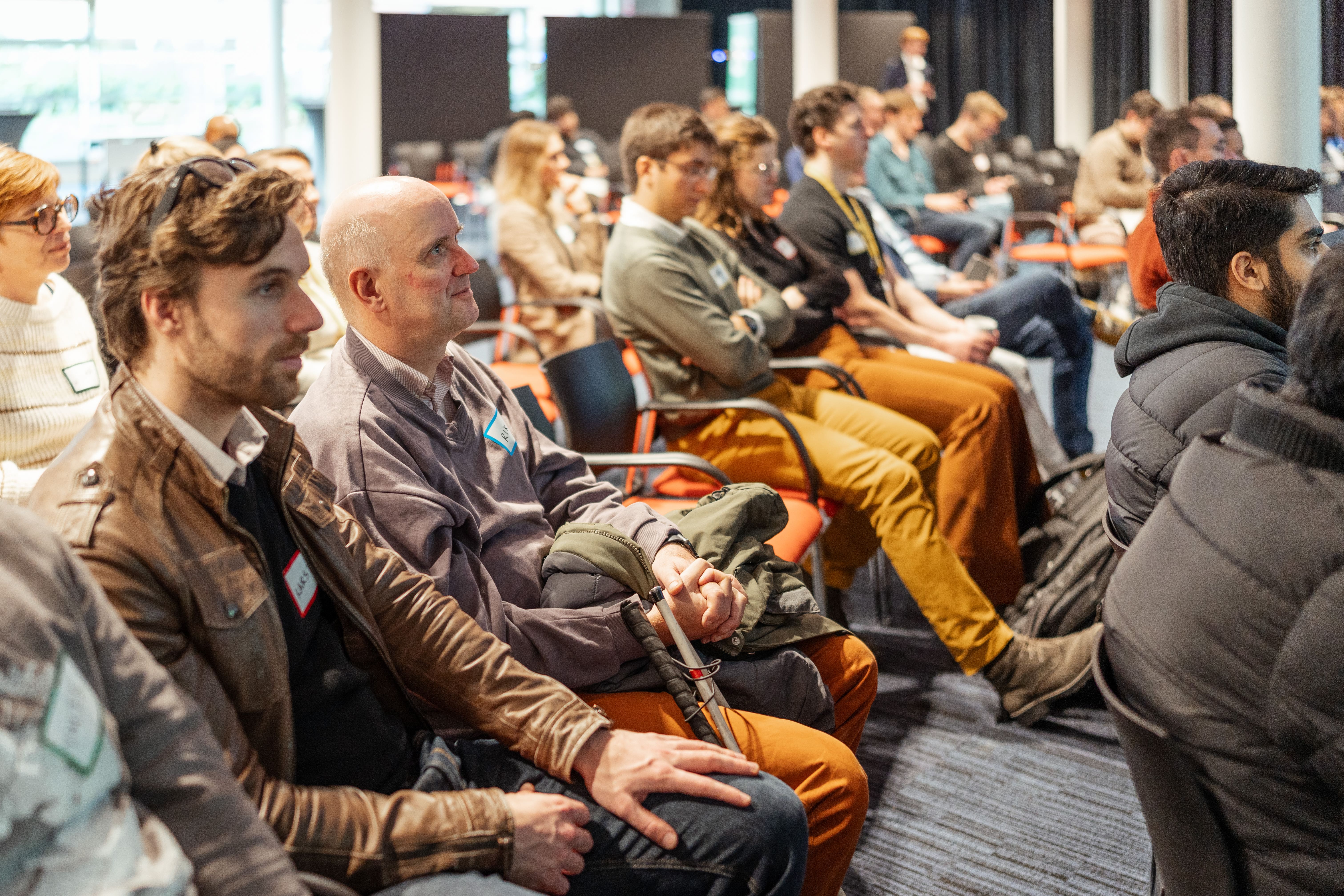 Adults seated attentively in a seminar or conference room, listening to a presentation.