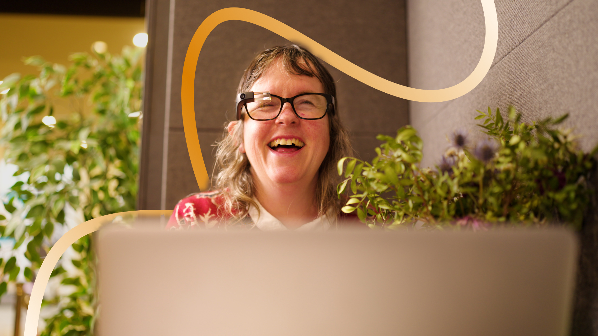 Ilona smailing in front of her laptop in a green office enviroment. 