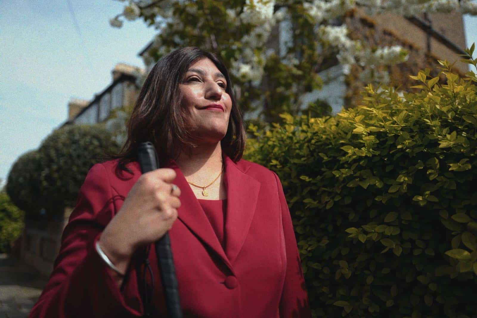 a photo of seema flowers with a red jacket and her walking cane in a green background