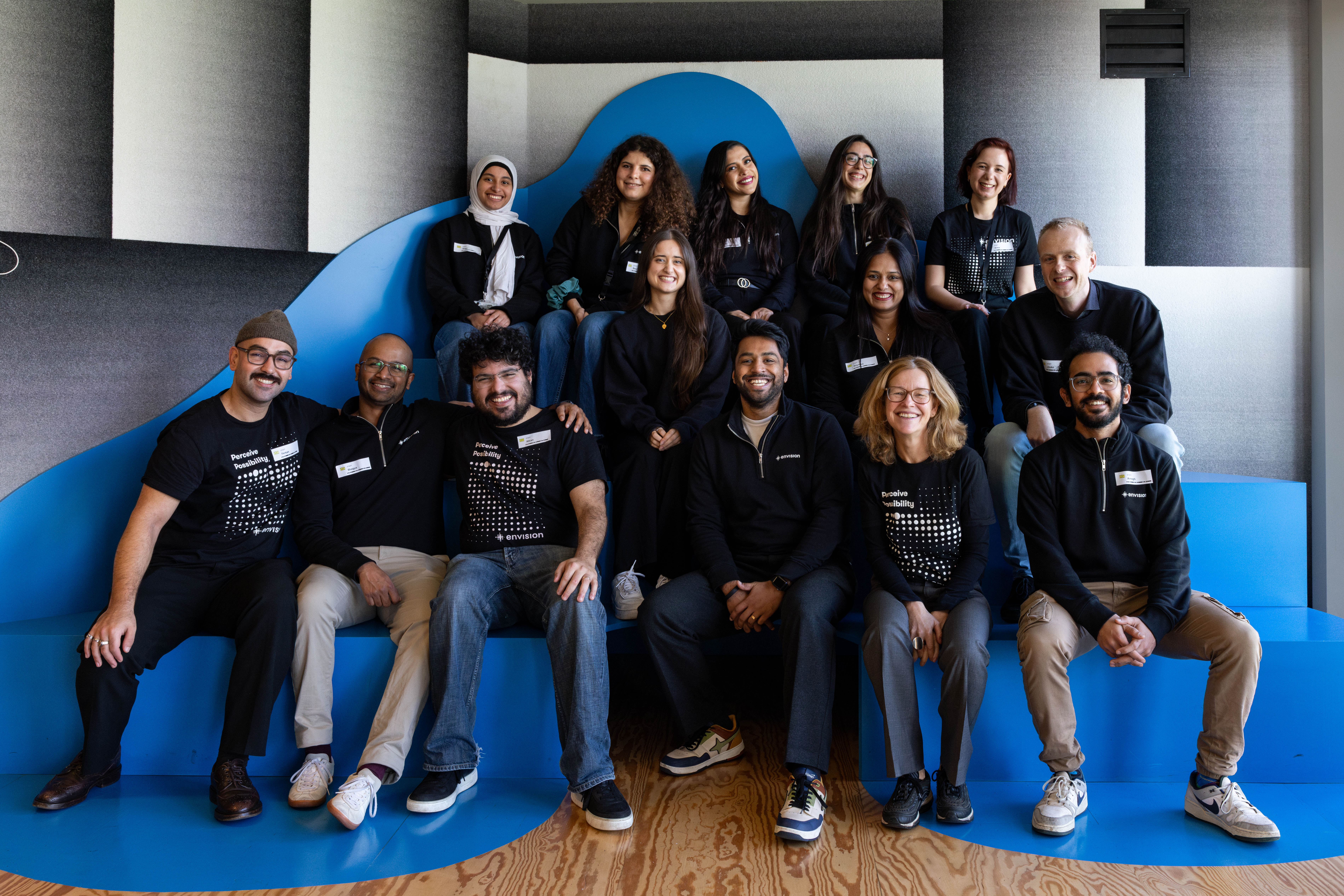 Team Envision posing in matching Envision sweatshirts while sitting on the steps of their office