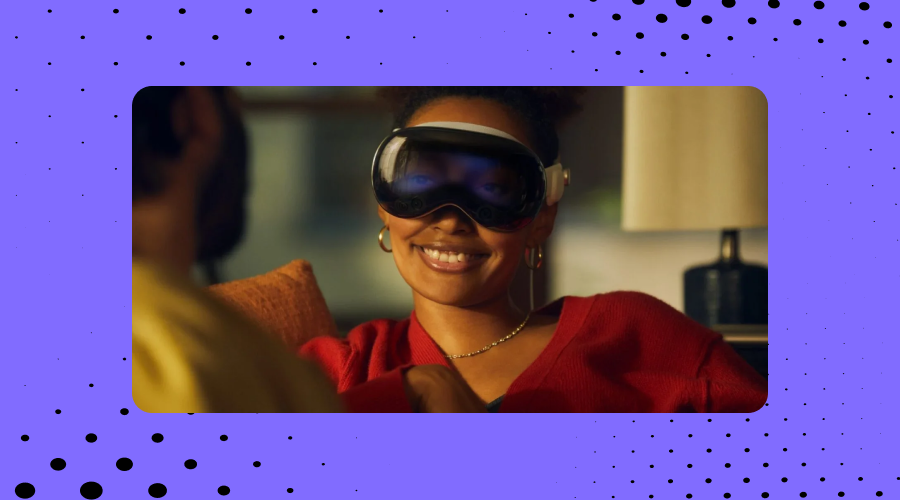A smiling woman wearing Apple Vision Pro's augmented reality glasses, with a blurred individual in the foreground, against a backdrop with a pattern of black dots referencing Envision's branding.