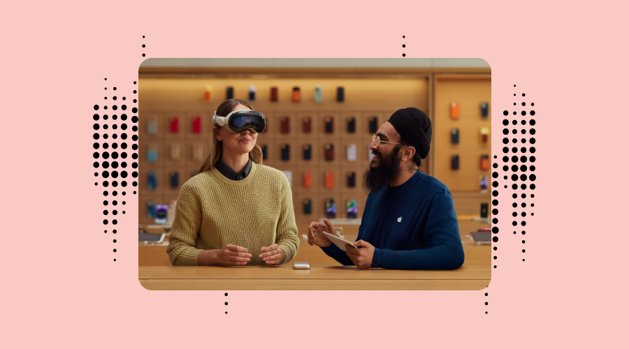 A woman wearing Apple Vision Pro is sitting across from a man in a blue shirt and turban who is holding a tablet. They are in an Apple Store with a wall of product shelves in the background.