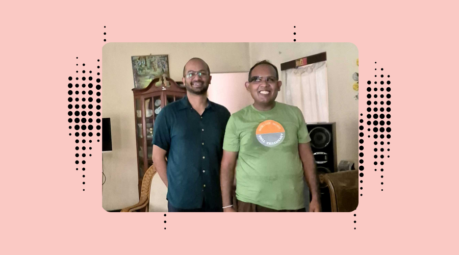 Two men smiling indoors, Bhagya from Envision is wearing a dark blue shirt and Janitha is in wearing green t-shirt and the Envision glasses. The background includes a wooden cabinet and a painting, with a pattern of black dots surrounding the image, representing Envision's branding.