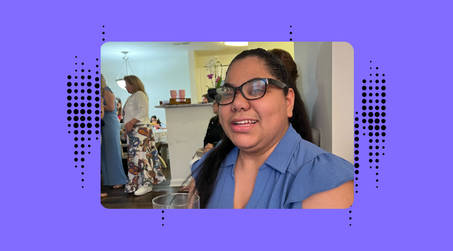 The background is purple with Envision dotted branding. Fernanda Da Silva, who  is wearing a blue top and Envision Glasses, smiles while seated indoors at a social gathering, holding a champagne flute. She wears a smartwatch and her hair is pulled back. The background is lively with people milling about and party decorations visible.
